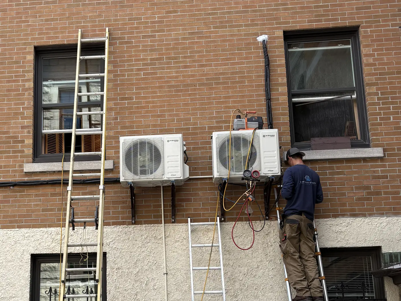 Avant : un frigoriste de Climativ installe les deux thermopompes murales sur la façade de brique