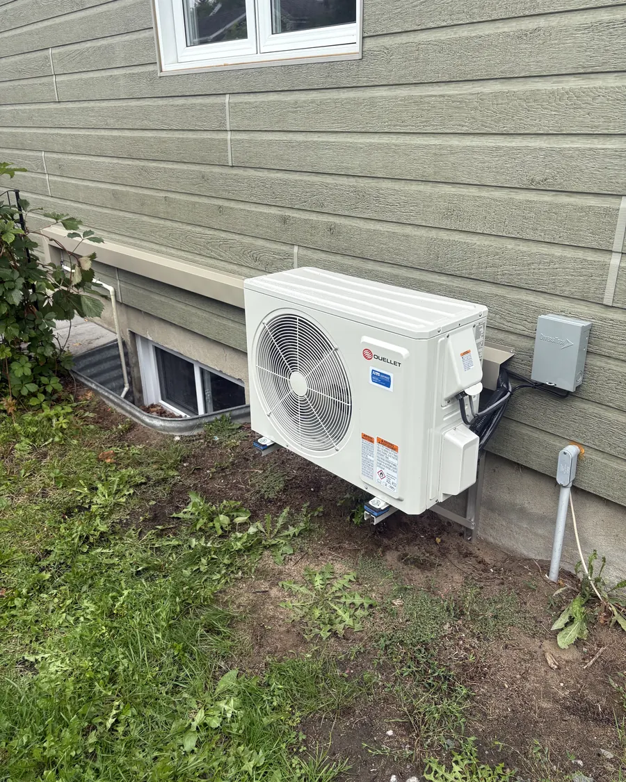 Thermopompe murale installée contre une maison au revêtement vert